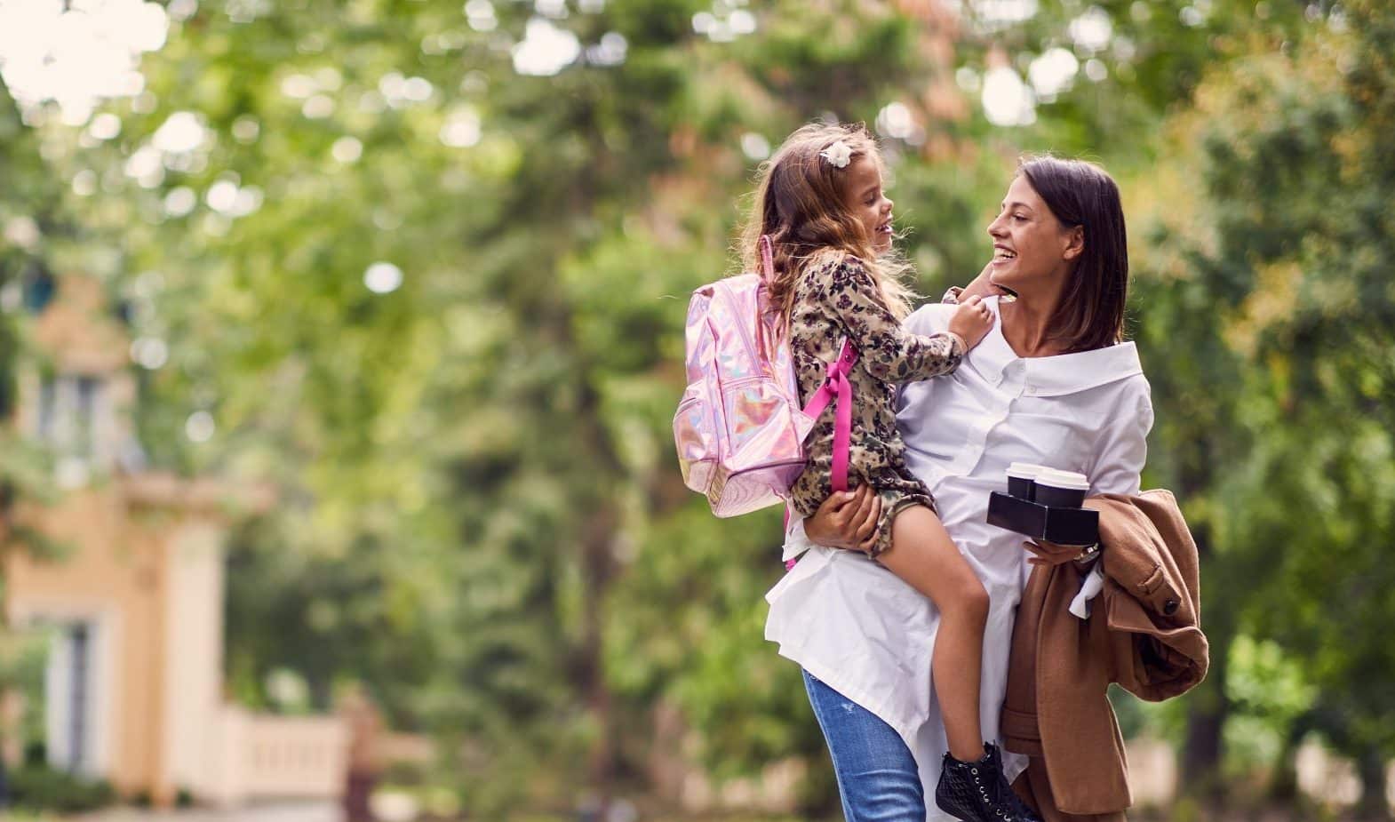 smiling mother holding a daughter with schoolbag