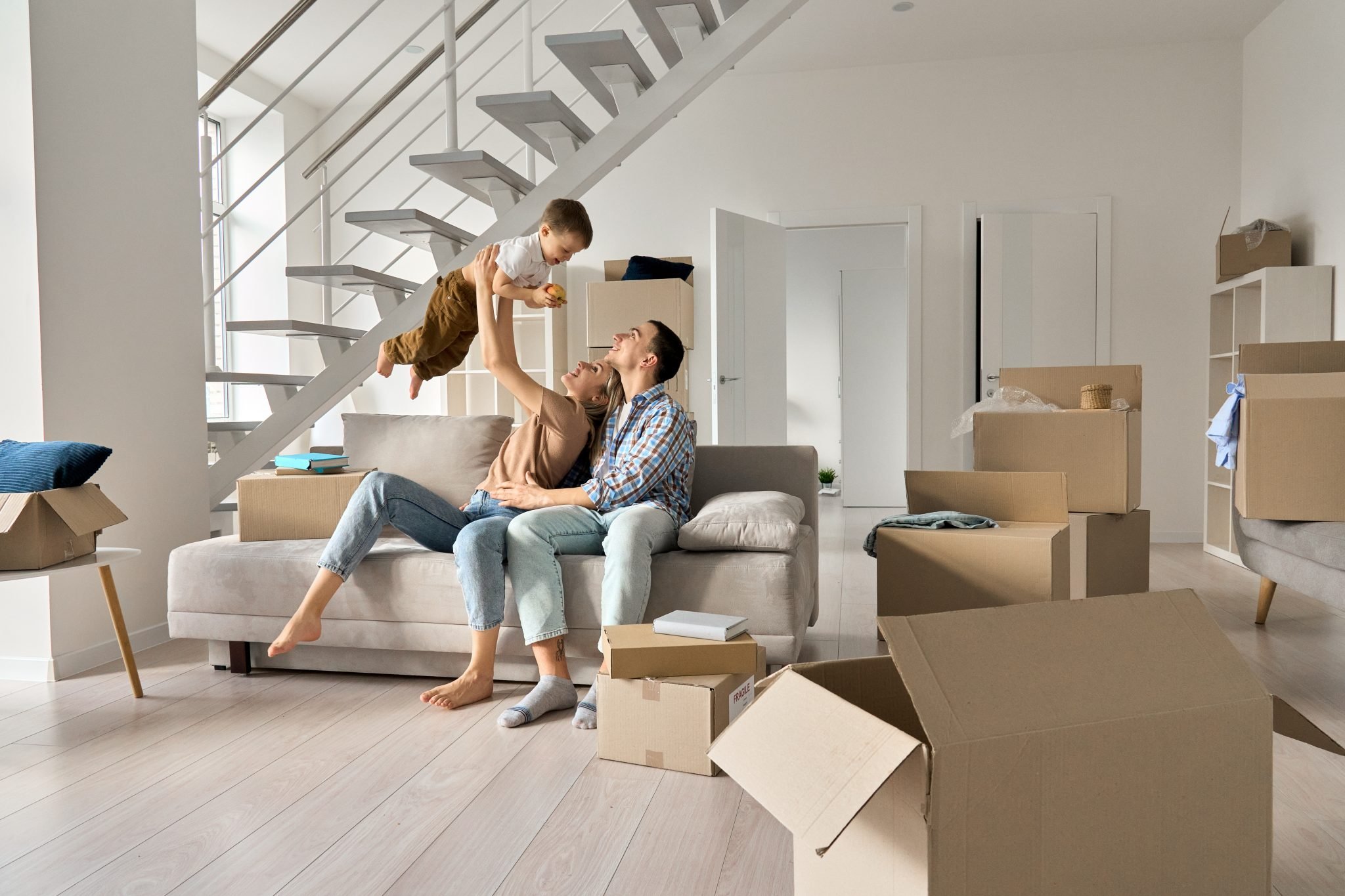 Happy young family playing with kid son together in new home on moving day.