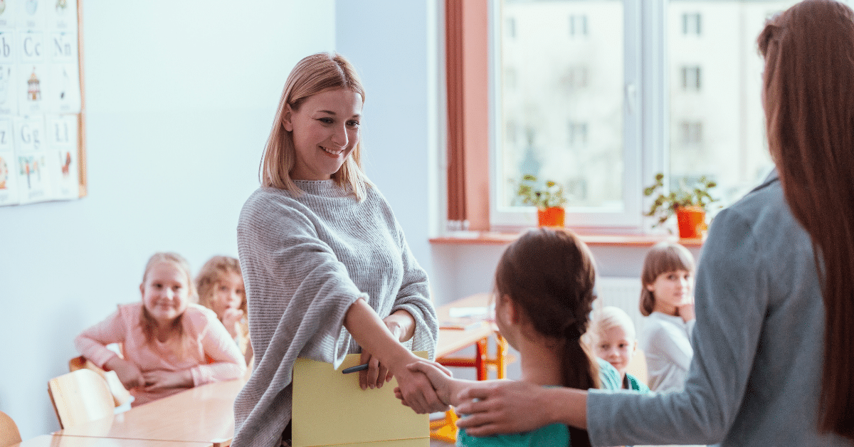 Midyear School Move – Teacher Welcoming New Student Teacher greeting a young student and her parent in a classroom during a midyear school transition