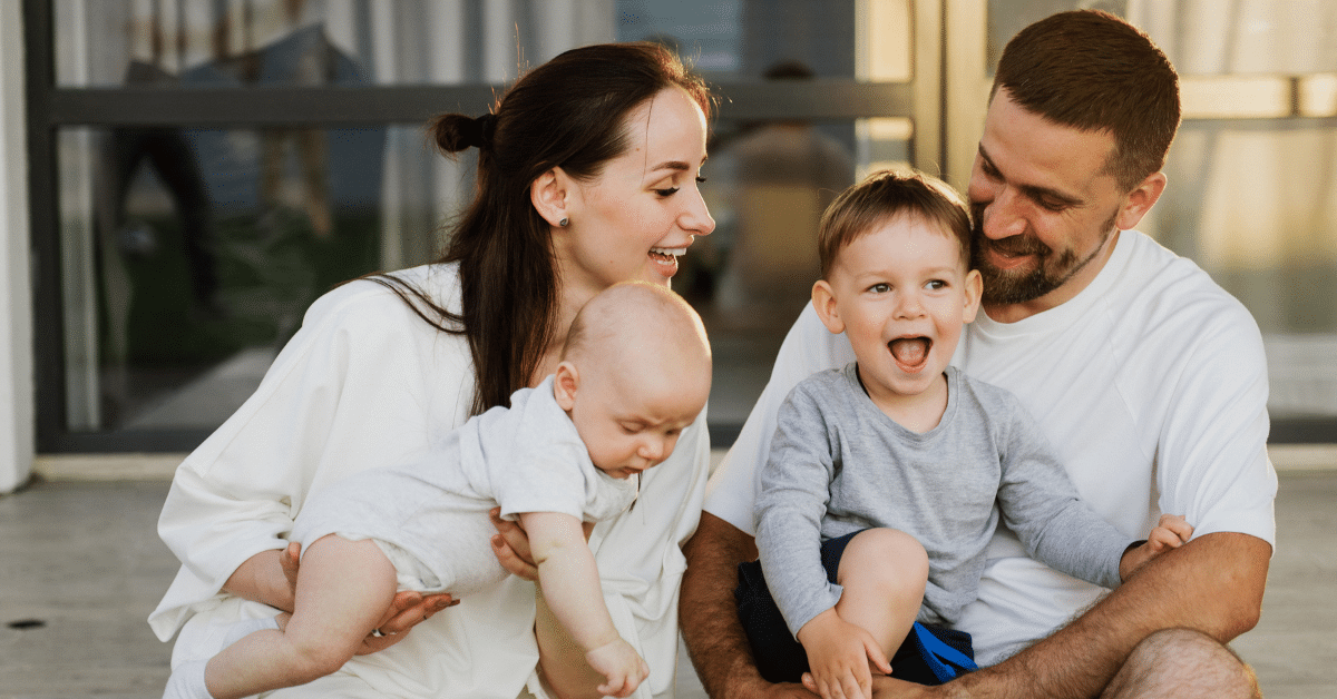 Family with two young children smiling together outside their new home after moving from NYC to the Philadelphia suburbs