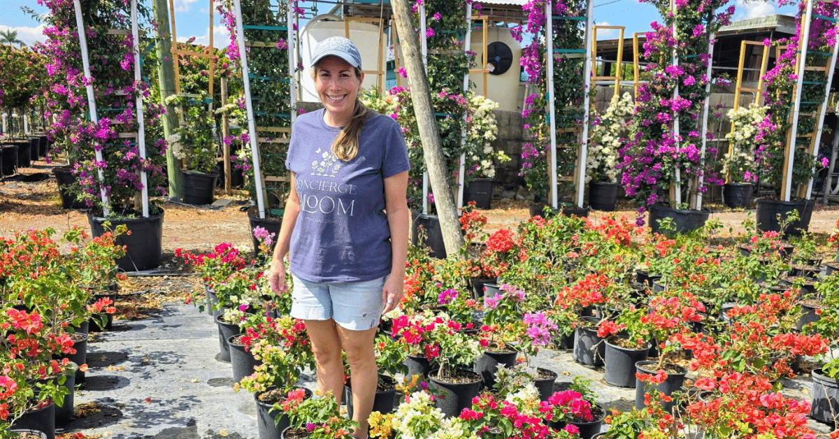 Cara Simon at Concierge Bloom Nursery Cara Simon standing among colorful potted plants at a nursery for her plantscaping business