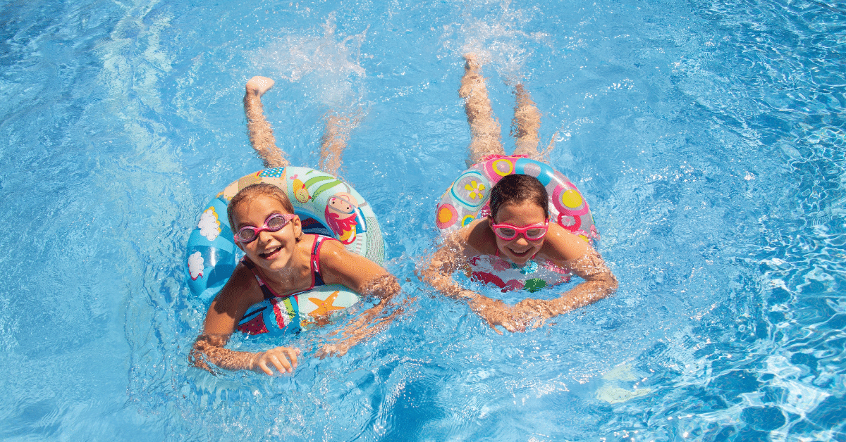 Summer Safety for Kids Two children wearing goggles float and play in a swimming pool on a sunny summer day.