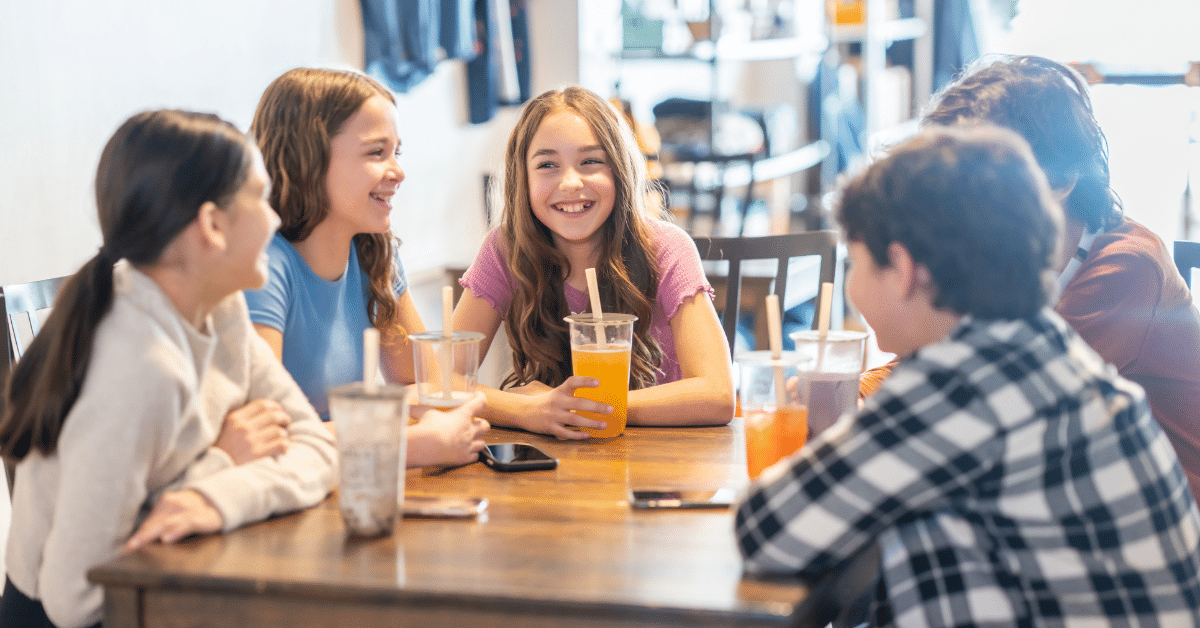 Tweens and Teens Socializing at a Café Group of tweens and teens sitting together at a café table, chatting and enjoying drinks.